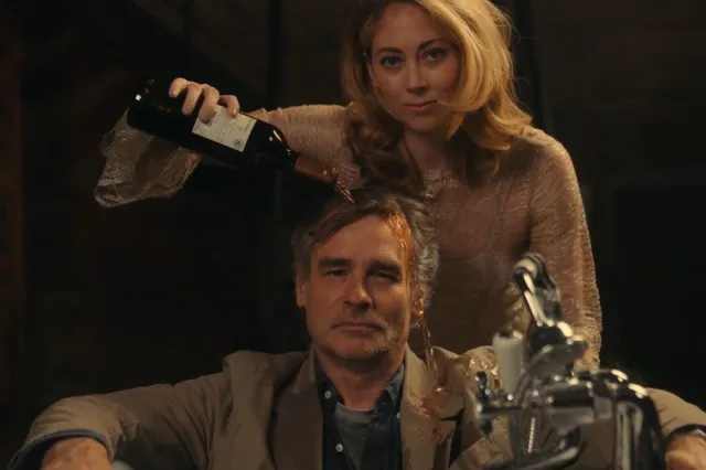 A woman pours a bottle of wine over a man's head
