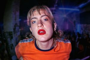 Close-up of a woman with blonde hair and bright red lipstick in a neon-lit club by colorful lights.