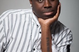 Portrait of a Black man in a striped shirt, resting his chin on his hand with a thoughtful expression.