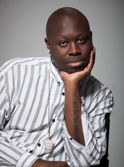 Portrait of a Black man in a striped shirt, resting his chin on his hand with a thoughtful expression.